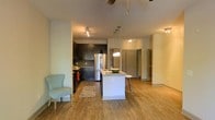 Located at 1040 Wake Towne Dr in Raleigh, NC, this single-floor residence offers a thoughtfully designed open-concept layout that seamlessly connects the kitchen and living areas. The kitchen is a standout feature, boasting dark cabinetry that contrasts beautifully with a white central island topped with a light countertop. Stainless steel appliances, including a full-sized refrigerator, add a sleek, modern touch, while pendant lighting over the island creates a warm and inviting atmosphere. The island also provides casual bar seating, making it ideal for dining or entertaining. Track lighting and a ceiling fan enhance both functionality and comfort throughout the space. Warm-toned hardwood-style flooring flows continuously across the entire floor, adding cohesion and a welcoming feel. The open living area offers generous room for furnishings and benefits from a light, neutral color palette on the walls that keeps the space feeling bright and airy. Multiple doorways lead to additional rooms, suggesting a well-organized floor plan with clear separation between living and private spaces. Overall, the residence combines contemporary design elements with practical, comfortable living in a clean and well-appointed setting.