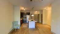 Located at 1040 Wake Towne Dr in Raleigh, NC, this single-floor residence offers a thoughtfully designed open-concept layout that seamlessly connects the kitchen and living areas. The kitchen is a standout feature, boasting dark cabinetry that contrasts beautifully with a white central island topped with a light countertop. Stainless steel appliances, including a full-sized refrigerator, add a sleek, modern touch, while pendant lighting over the island creates a warm and inviting atmosphere. The island also provides casual bar seating, making it ideal for dining or entertaining. Track lighting and a ceiling fan enhance both functionality and comfort throughout the space. Warm-toned hardwood-style flooring flows continuously across the entire floor, adding cohesion and a welcoming feel. The open living area offers generous room for furnishings and benefits from a light, neutral color palette on the walls that keeps the space feeling bright and airy. Multiple doorways lead to additional rooms, suggesting a well-organized floor plan with clear separation between living and private spaces. Overall, the residence combines contemporary design elements with practical, comfortable living in a clean and well-appointed setting.