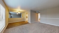 This well-appointed one-bedroom, one-bathroom unit is thoughtfully laid out across a single floor, making efficient use of its space. The main living area features warm-toned carpet underfoot, a decorative chair rail along the walls, and a front entry door flanked by a large window that fills the room with natural light. A mirrored wall in the dining area enhances the sense of openness, while a pendant chandelier overhead adds a classic decorative touch. The dining area transitions seamlessly into the galley-style kitchen, which is equipped with white cabinetry, stone-patterned countertops, and light hardwood-style flooring. A pass-through connects the kitchen visually to the dining and living spaces, promoting an open and connected feel throughout. The bedroom is generously sized, finished with plush carpet, neutral-toned walls, a ceiling fan with integrated lighting, and a window with a view of surrounding greenery. The full bathroom features a white tiled tub-shower combination with chrome fixtures and hardwood-style flooring, offering a clean and functional design. Throughout the unit, neutral color palettes and consistent finishes create a cohesive and move-in-ready atmosphere.