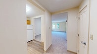 Located at 44 School St in Weston, MA, this single-floor, 2-bedroom, 1-bathroom residence offers a well-organized layout with a warm, neutral aesthetic throughout. The open living area features light gray carpeting and cream-toned walls, creating a clean, bright atmosphere. A hallway connects the living space directly to the kitchen, fostering a cohesive flow between rooms.

The kitchen is well-appointed with warm honey-toned wood cabinetry, light granite-style countertops, and white appliances including a range, refrigerator, and dishwasher. Light hardwood-style flooring adds a polished finish to this functional cooking space.

The spacious primary bedroom offers generous room to accommodate a variety of furniture arrangements, with soft carpeting underfoot and windows that frame views of surrounding greenery. The second bedroom is similarly carpeted and benefits from natural light through dual windows overlooking lush outdoor foliage.

The bathroom is designed with accessibility in mind, featuring a roll-in shower area with stainless steel grab bars, white tile flooring, and a vanity with matching wood cabinetry and granite-style countertop. Two hallways provide efficient circulation throughout the unit. Overall, the residence presents a comfortable, functional living environment in a serene Weston setting.