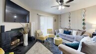 This efficiently designed one-bedroom, one-bathroom home makes excellent use of its single-floor layout, offering a comfortable and cohesive living experience. The combined living and dining area serves as the heart of the home, where the living room features plush carpeting, a ceiling fan with light fixture, a tiled wood-burning fireplace, a wall-mounted television, and sliding glass doors framed by vertical blinds that invite natural light. Decorative mirror panels accent the neutral-toned walls, adding visual depth to the space. Adjacent to the living area, the dedicated dining nook accommodates a round table with seating for four, decorated with tasteful wall art. The kitchen is efficiently arranged with warm wood-toned cabinetry, light-colored countertops, stainless steel appliances including a refrigerator and dishwasher, and durable wood-look flooring. The bedroom offers a quiet retreat with carpeted flooring, a ceiling fan, a window with blinds for natural light and privacy, and a textured ceiling consistent throughout the home. The bathroom features a wood-vanity with single-sink, a large mirror with overhead lighting, and wood-look flooring. Each room reflects a warm, functional design suited for comfortable everyday living.