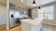This thoughtfully designed 2-bedroom, 2-bathroom residence offers a clean, modern aesthetic across a single floor. The open-concept living and kitchen area serves as the heart of the home, featuring light wood-look flooring, recessed lighting, and sleek pendant lights. The kitchen is outfitted with gray cabinetry, a white quartz waterfall island with an undermount sink, a subway tile backsplash, and stainless steel appliances including a French door refrigerator and built-in microwave. Natural light flows in through windows with blinds, enhancing the bright, airy atmosphere.

The primary bedroom is generously sized with light wood flooring, multiple windows, and direct access to its private en-suite bathroom. The primary bath features a double-sink vanity with navy blue cabinetry, white countertops, a glass-enclosed walk-in shower with large-format tile, and wood-look flooring. The second bedroom offers plush carpeting and natural light, accompanied by a full bathroom with a soaking tub, tiled surround, and a stylish vanity. Both bedrooms include dedicated closets, one of which is a walk-in with built-in shelving and hanging rods. A connecting hallway ties the layout together efficiently.