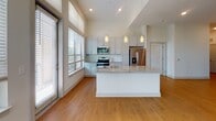 Located at 1715 Legion Rd in Chapel Hill, NC, this single-floor residence offers a thoughtfully designed layout characterized by clean lines, neutral tones, and an abundance of natural light throughout. The open-concept living area impresses with soaring ceilings and expansive floor-to-ceiling windows, allowing sunlight to pour in while framing views of the surrounding tree canopy. A sliding glass door provides direct outdoor access, further enhancing the bright, airy atmosphere. Warm hardwood-style flooring runs throughout the main living spaces, complementing the contemporary aesthetic.

The kitchen is a standout feature, anchored by a large central island with granite countertops, white cabinetry, a tile backsplash, and stainless steel appliances including a refrigerator, range, and microwave. Generous windows above the counters continue the theme of natural light.

The bathrooms are well-appointed, each featuring granite vanity countertops, white cabinetry, and large framed mirrors. The primary bathroom includes a walk-in glass-enclosed shower with marble-style tile surround. Multiple walk-in closets with wire shelving systems offer substantial storage capacity. The bedrooms are comfortably scaled, with large windows offering peaceful wooded views and a mix of hardwood-style and carpeted flooring.