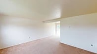 This two-floor residential space offers a functional and practical layout designed for everyday living. The main living area is generously sized, featuring warm beige carpet, neutral white walls, and a textured ceiling that adds subtle dimension. A structural beam accent and a large window at the far end of the living room allow natural light to fill the space, creating an open and airy atmosphere.

The kitchen is equipped with warm oak cabinetry, laminate countertops, and white appliances including a gas range and a full-size refrigerator. It connects seamlessly to the adjoining living area, supporting an easy flow between spaces.

The bedrooms are carpeted and bright, each featuring windows that bring in natural light and views of the surrounding neighborhood. Closet storage is provided in the bedrooms, adding practicality to the living quarters.

The bathroom is finished with white tile surround, a tub-shower combination, a wood-vanity with an integrated sink, a large mirror with vanity lighting, and a window for natural ventilation.

A lower-level utility area houses the mechanical systems, including visible plumbing, piping, and an electrical panel, reflecting the functional infrastructure of the building. An entry area with a door, side window, and staircase connects the two floors, completing the layout of this straightforward and well-structured space.