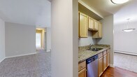 Located at 1722 Poplar Pl in Schaumburg, Illinois, this single-floor, two-bedroom, one-bathroom home offers a well-organized layout with comfortable living spaces throughout. The kitchen is outfitted with granite countertops, light maple cabinetry, a stainless steel undermount sink, and a dishwasher, with hardwood-style flooring adding a warm contrast. Adjacent to the kitchen, the dining area flows naturally into the living room, which features plush carpeting, a wall-mounted air conditioning unit, and a large sliding glass door framed by vertical blinds that opens to a balcony with views of surrounding greenery, filling the space with natural light. Both bedrooms are carpeted, with the generously sized primary bedroom featuring a closet, a window with outdoor views, and a baseboard heating system. The second bedroom offers a clean, neutral palette with soft carpet. The bathroom includes granite-style countertops, a large vanity mirror, bright overhead lighting, and a tiled tub-shower combination. Connecting hallways provide efficient circulation throughout the home. The overall ambiance is clean, neutral, and functional, making this a practical and comfortable residence in the heart of Schaumburg.