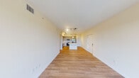 This single-floor unit features a clean, contemporary design with light-toned hardwood-style flooring and neutral walls throughout, creating a bright and cohesive aesthetic. The open-concept living area flows seamlessly into the kitchen, which serves as the focal point of the space. The kitchen is well-appointed with light wood shaker-style cabinetry accented by matte black hardware, white subway tile backsplash, quartz countertops, a central island, and a full suite of stainless steel appliances including a side-by-side refrigerator, electric range, built-in microwave, and dishwasher. Track lighting and a pendant fixture illuminate the kitchen effectively. The living area is generously proportioned, with a sliding glass door opening to a private balcony that offers views of surrounding greenery. A secondary bedroom features a window with similar outdoor views and ample natural light. The primary bathroom includes a dual-sink vanity with quartz countertops, white cabinetry with built-in storage, a large mirror, and a walk-in shower. A second bathroom provides a tub-shower combination and tile flooring. The entry area offers additional closet access, completing the functional layout.