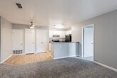 This single-floor residential unit offers a practical and well-organized layout designed for comfortable everyday living. The open-concept living and dining area is finished with plush grey carpet and neutral grey walls, creating a clean and cohesive atmosphere. A ceiling fan adds both function and comfort to the main living space, which also features a window with vertical blinds, allowing natural light to filter in.

The kitchen is efficiently designed with white shaker-style cabinetry, dark speckled countertops, and wood-look flooring that adds warmth to the space. Stainless steel appliances include an electric range and a full-size refrigerator, complemented by an under-cabinet range hood and a stainless steel sink. A peninsula counter connects the kitchen to the living area, providing additional prep space and a natural transition between the two zones.

The bedrooms are carpeted and generously proportioned, each featuring neutral grey walls, windows with vertical blinds for natural light, and ample wall space. The bathroom is clean and functional, featuring a full-size soaking tub with shower combination, chrome fixtures, a white vanity with a dark countertop, and wood-look tile flooring. The textured walls throughout add subtle dimension to the overall interior aesthetic.