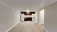 Located at 4941 Central Drive in Stone Mountain, Georgia, this efficiently designed one-bedroom, one-bathroom residence offers a practical and comfortable layout across a single floor. The open-concept kitchen and living area form the heart of the unit, featuring light wood-style luxury vinyl flooring, neutral gray walls, and a textured ceiling that adds subtle character throughout. The kitchen is equipped with rich dark-cherry cabinetry, a white electric range, a full-size refrigerator, and a single-basin sink with stone-look countertops — all neatly arranged along one wall to maximize the open feel of the combined living space. A front-facing window in the living area brings in natural light and provides views of the surrounding greenery, while a front entry door offers convenient direct access. A hallway connects the main living area to the private bedroom, which features plush carpeting, a ceiling fan with light fixture, a natural-light window, crown molding, and a spacious double-door closet with built-in shelving and hanging rods. The full bathroom includes a dark-cabinetry vanity with a white countertop, a toilet, and a tub/shower combination. A dedicated utility area houses the water heater, rounding out this well-organized and functional home.