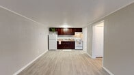 Located at 4941 Central Drive in Stone Mountain, Georgia, this efficiently designed one-bedroom, one-bathroom residence offers a practical and comfortable layout across a single floor. The open-concept kitchen and living area form the heart of the unit, featuring light wood-style luxury vinyl flooring, neutral gray walls, and a textured ceiling that adds subtle character throughout. The kitchen is equipped with rich dark-cherry cabinetry, a white electric range, a full-size refrigerator, and a single-basin sink with stone-look countertops — all neatly arranged along one wall to maximize the open feel of the combined living space. A front-facing window in the living area brings in natural light and provides views of the surrounding greenery, while a front entry door offers convenient direct access. A hallway connects the main living area to the private bedroom, which features plush carpeting, a ceiling fan with light fixture, a natural-light window, crown molding, and a spacious double-door closet with built-in shelving and hanging rods. The full bathroom includes a dark-cabinetry vanity with a white countertop, a toilet, and a tub/shower combination. A dedicated utility area houses the water heater, rounding out this well-organized and functional home.