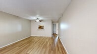 This single-floor residence offers a clean, functional layout with a cohesive neutral color palette and warm hardwood-style flooring that flows throughout the main living areas. The generous living room is brightened by natural light filtering through large windows dressed with blinds, and a ceiling fan adds both style and comfort overhead. A pass-through window connects the living area to the kitchen, enhancing the open feel of the space. The galley-style kitchen is efficiently designed with gray cabinetry lining both walls, laminate countertops, a stainless steel sink, an electric range, a dishwasher, and a tile mosaic backsplash accent. Light ceramic tile flooring completes the kitchen's practical finish. A hallway leads to the bedroom, which features its own ceiling fan, a sun-filled window, and dual reach-in closets with louvered bifold doors offering ample storage with built-in shelving and hanging rods. The bathroom includes a full-size soaking tub with an overhead shower, a vanity with cabinet storage, and tile flooring. Additional built-in shelving is visible in the hallway, providing convenient storage. Textured ceilings are present throughout, contributing to the space's classic residential character.