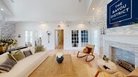 Located at 1900 Switzer Rd in Gulfport, Mississippi, this single-floor community space for The Bayou District is thoughtfully designed with a coastal-modern aesthetic that blends warmth and sophistication. The primary living room immediately impresses with soaring vaulted ceilings and a dramatic stacked-stone fireplace wall that anchors the room. Arched transom windows above French doors flood the space with natural light, while crisp white shiplap walls and light hardwood flooring create a clean, airy atmosphere throughout. A second living area offers a more intimate setting, featuring a tray ceiling with recessed lighting, additional shiplap detailing, built-in shelving, and French doors that connect the two rooms seamlessly. This flex space accommodates lounge seating as well as a high-top dining table and bar stools set against a stone accent wall with a wall-mounted television. The kitchenette is finished with shaker-style cabinetry, marble-look countertops, a stainless steel sink, and eye-catching black-and-white patterned tile flooring that adds a distinctive design touch. Together, the rooms offer a cohesive, welcoming environment well-suited for community gatherings and events.