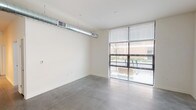 Located at 705 E Walnut St in Indianapolis, Indiana, this modern single-floor unit showcases a clean, industrial-contemporary aesthetic throughout. Polished concrete floors run continuously across the entire space, lending a sleek, cohesive look that complements the crisp white walls and minimalist design sensibility.

The open living areas are bathed in natural light, courtesy of expansive floor-to-ceiling windows fitted with horizontal blinds, offering views of the surrounding urban streetscape. Exposed cylindrical ductwork runs along the ceiling in the main living area, adding an industrial character that defines the overall ambiance.

The kitchen is well-appointed with rich, dark espresso cabinetry extending to the ceiling for generous storage, paired with light countertops and a full suite of black appliances including a refrigerator, range, built-in microwave, and dishwasher. The layout flows efficiently into the adjoining living and corridor spaces.

Multiple rooms offer flexible use, each featuring the same polished concrete flooring and large windows that invite ample daylight and neighborhood views. A dedicated bathroom features gray tile wainscoting along the lower walls, a wall-mounted sink, a vanity mirror, and accessible fixtures, maintaining the space's modern utilitarian character. A central hallway connects the various rooms, creating a practical and well-organized floor plan throughout.