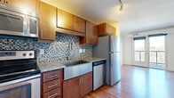 This efficiently designed one-bedroom, one-bathroom unit offers a smart and functional layout across a single floor. The open-concept living and kitchen area is anchored by warm hardwood flooring that extends throughout the main living spaces, creating a cohesive and inviting atmosphere. The kitchen is a standout feature, showcasing rich wood cabinetry, granite countertops, and a striking mosaic tile backsplash in muted blue and gray tones. A deep stainless steel farmhouse sink, stainless steel refrigerator, dishwasher, range, and built-in microwave complete the fully equipped culinary space. Track lighting overhead adds a modern, industrial touch. The living area benefits from an open connection to the kitchen, providing a versatile space for daily living. The bedroom offers a comfortable footprint, carpeted flooring for warmth, and a large window that fills the room with natural light and frames outdoor views of the surrounding neighborhood. The bathroom features a full tub-shower combination, tile flooring, a vanity with granite countertop, and clean white walls that lend a bright, functional feel. Exposed ductwork in select areas adds an urban, loft-inspired character to the overall aesthetic of this thoughtfully laid-out unit.