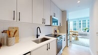 Located at 180 Morgan Street in Jersey City, NJ, this thoughtfully designed one-bedroom, one-bathroom residence offers a refined modern living experience across a single floor. The open layout maximizes every inch of space, with light wood flooring and a crisp white palette creating a cohesive, airy atmosphere throughout.

The kitchen is outfitted with floor-to-ceiling white cabinetry, white quartz countertops, a textured tile backsplash, and stainless steel appliances, all accented by striking matte black hardware and a sleek black pull-down faucet. The galley-style design is both functional and visually polished.

The spacious primary bedroom is a standout feature, dominated by expansive floor-to-ceiling windows that frame dramatic city skyline views, flooding the room with natural light. Light wood flooring continues here, complementing the bright, open ambiance.

The living area provides a welcoming lounge space with clean white walls, recessed lighting, and a seamless connection to the kitchen and bedroom zones.

The bathroom features large-format white tile flooring, a white vanity with an illuminated mirror, matte black fixtures, and a full tiled shower, delivering a clean, contemporary aesthetic. A hallway connects the rooms efficiently, completing this well-appointed urban residence.