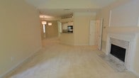 This single-floor residence offers an open-concept layout that seamlessly connects the main living, dining, and kitchen areas, creating a fluid and functional living environment. The expansive main living area is finished with plush wall-to-wall carpeting in a neutral tone, providing a warm and inviting atmosphere throughout. Soft, cream-colored walls complement the light palette, enhancing the overall sense of openness.

The dining area is distinguished by an elegant pendant lighting fixture, adding a refined touch to the space. It flows naturally into the kitchen, which features a raised breakfast bar, dark countertops, white cabinetry, and built-in appliances including an oven — offering both style and practicality. The kitchen's layout is efficient, with ample counter and storage space.

A doorway near the main living area leads to additional rooms, hinting at a well-organized floor plan. Near the entryway, tile flooring transitions from the carpeted living space, adding a practical and visually interesting detail. The residence is well-lit with a combination of natural light and overhead fixtures, contributing to a bright and comfortable ambiance throughout the home.