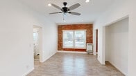 Located at 1057 S Western Ave in Los Angeles, this single-floor unit blends classic character with modern updates throughout. The main living area makes an immediate impression with its striking exposed brick accent wall, which adds warmth and texture against the crisp white walls and ceilings. Wood-look flooring runs consistently throughout, complementing the bright, airy feel of the space. Recessed lighting and a contemporary ceiling fan with sleek blades ensure the room stays well-lit and comfortable year-round. Natural light filters in through a front-facing window framed by the exposed brick, offering views of the surrounding neighborhood. An open entryway area with clean white walls and light flooring provides a welcoming transition into the living space. The kitchen features white shaker-style cabinetry, a stainless steel refrigerator, and a window overlooking the exposed brick wall, creating a functional and visually cohesive cooking space. The bathroom is finished in an all-white palette, complete with a tub-shower combination, white tile surround, a window for natural ventilation, a single vanity with chrome fixtures, and a mirrored medicine cabinet. The overall layout is straightforward and efficient, with arched doorway details adding a subtle architectural touch throughout.