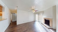 This single-floor residence offers a well-organized layout with a combination of hardwood-style and carpeted flooring throughout. The living room serves as the central gathering space, highlighted by a brick-surround wood-burning fireplace, a ceiling fan with light fixture, and a textured ceiling. A sliding glass door floods the room with natural light and provides direct access to the outdoors, while vertical blinds offer privacy control. The open flow connects the living area to a dedicated dining space, which transitions seamlessly into a galley-style kitchen. The kitchen is equipped with warm honey-toned wood cabinetry, black appliances including a range, microwave, refrigerator, and dishwasher, all set over durable hardwood-style flooring. The bedrooms are carpeted for comfort, each featuring ceiling fans and windows that allow natural light. The primary bedroom includes an en-suite vanity area with a single-basin sink, wood cabinetry, and an adjacent walk-in closet. A full bathroom is also present, complete with a tub-shower combination, tile surround, wood vanity cabinetry, and hardwood-style flooring. Throughout the space, white walls and textured ceilings provide a clean, neutral backdrop.