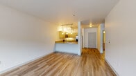 This efficiently designed 1-bedroom, 1-bathroom residence offers a thoughtful single-floor layout across five distinct spaces, including a living room, kitchen, bedroom, bathroom, and closet. The open-concept living and kitchen area is anchored by warm wood-style flooring and clean white walls that create a bright, welcoming atmosphere. The kitchen is a standout feature, boasting light maple cabinetry, granite-look countertops, a peninsula with a double stainless steel sink, and a full suite of stainless steel appliances including a refrigerator with ice maker, electric range, built-in microwave, and dishwasher. Pendant and track lighting overhead adds both function and a modern touch. The living area flows seamlessly from the kitchen, offering a comfortable and versatile space. The bedroom features plush carpeting, a wall-mounted climate control unit, and windows that bring in natural light with views of surrounding greenery. The bathroom is finished with matching light cabinetry, granite-look countertops, a large mirror, and a tiled tub-shower combination. Wood-style flooring continues into the bathroom, reinforcing the cohesive design aesthetic found throughout this well-organized and move-in-ready residence.