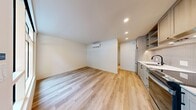 Located at 2517 Eastlake Ave E in Seattle, WA, this thoughtfully designed unit maximizes every inch of its single-floor layout. Light oak hardwood flooring runs continuously throughout, creating a cohesive and airy feel. The open living area is bright and clean, featuring recessed lighting, smooth white walls, and a wall-mounted mini-split HVAC unit for year-round climate control.

The kitchen is well-appointed with light wood shaker-style cabinetry, open upper shelving, a vertical tile backsplash, white quartz countertops, a stainless steel refrigerator, and a stainless range with overhead ventilation hood. A large floor-to-ceiling window and glass entry door flood the kitchen with natural light and provide a view of a lush, landscaped courtyard.

The bathroom features a full soaking tub with a subway tile surround, matte black fixtures, and the same warm hardwood flooring carried throughout the unit. A dedicated laundry closet houses a stacked washer and dryer, while an adjacent walk-in closet offers organized storage with built-in shelving and a clothing rod. Two hallway areas connect the spaces seamlessly, contributing to an efficient and functional layout overall.