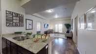 This single-floor residence offers a thoughtfully designed open-concept layout that seamlessly connects the kitchen and living areas. The kitchen is equipped with dark espresso cabinetry, granite countertops, a undermount sink, and black appliances, including a full-size refrigerator and range. The adjoining living room is bright and inviting, featuring hardwood-style flooring, neutral walls, and French doors that open to a private outdoor space, allowing natural light to fill the room.

The bedrooms are carpeted and generously sized, each with window treatments providing natural light and privacy. The primary bedroom connects to a spacious walk-in closet and an en-suite bathroom outfitted with dark cabinetry, granite countertops, a large mirror with vanity lighting, and a walk-in shower. A second full bathroom mirrors the same refined finishes and serves the additional rooms.

A versatile flex room, currently arranged as a home office, features carpet flooring, a window with outdoor views, and ample space for a variety of uses. The in-unit laundry area houses a full-size side-by-side washer and dryer with overhead wire shelving for added storage. Throughout the residence, consistent design elements — including granite surfaces, dark cabinetry, and neutral tones — create a cohesive and polished aesthetic.