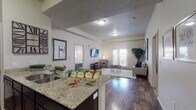 This single-floor residence offers a thoughtfully designed open-concept layout that seamlessly connects the kitchen and living areas. The kitchen is equipped with dark espresso cabinetry, granite countertops, a undermount sink, and black appliances, including a full-size refrigerator and range. The adjoining living room is bright and inviting, featuring hardwood-style flooring, neutral walls, and French doors that open to a private outdoor space, allowing natural light to fill the room.

The bedrooms are carpeted and generously sized, each with window treatments providing natural light and privacy. The primary bedroom connects to a spacious walk-in closet and an en-suite bathroom outfitted with dark cabinetry, granite countertops, a large mirror with vanity lighting, and a walk-in shower. A second full bathroom mirrors the same refined finishes and serves the additional rooms.

A versatile flex room, currently arranged as a home office, features carpet flooring, a window with outdoor views, and ample space for a variety of uses. The in-unit laundry area houses a full-size side-by-side washer and dryer with overhead wire shelving for added storage. Throughout the residence, consistent design elements — including granite surfaces, dark cabinetry, and neutral tones — create a cohesive and polished aesthetic.