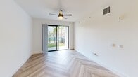 This thoughtfully designed 2-bedroom, 1-bathroom residence in Royal Palm Beach, Florida, offers a clean, modern aesthetic throughout its single-floor layout. A striking herringbone-patterned wood floor runs consistently through every room, creating a cohesive and visually dynamic foundation across the entire space.

The open-concept kitchen and living area serves as the heart of the home. The kitchen is outfitted with light wood cabinetry, stainless steel appliances including a full-size refrigerator, microwave, and range, and a sleek white quartz island with an undermount sink. Stylish globe pendant lights in brushed gold add a contemporary touch and illuminate the workspace effectively. Track lighting overhead provides additional coverage throughout the living area.

Both bedrooms are bright and well-proportioned, each featuring ceiling fans and crisp white walls. The primary bedroom is notably spacious and opens directly to the outdoors through floor-to-ceiling sliding glass doors, offering views of a landscaped exterior with palm trees. The second bedroom features a window with blinds, filling the room with natural light.

The bathroom is finished with large-format tile in the tub/shower surround, a wood-toned vanity with a white countertop, and a backlit mirror that adds a modern, polished detail. A dedicated hallway and closet round out the functional layout of this well-appointed residence.