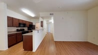 Located at 2400 E Llano Estacado Blvd in Clovis, New Mexico, this single-floor residence offers a clean, functional layout designed for comfortable everyday living. The open-concept floor plan seamlessly connects the kitchen and living area, creating a bright and airy atmosphere throughout. The kitchen is equipped with dark wood cabinetry, black appliances including a range and microwave, and a granite-style countertop that extends into a breakfast bar, providing both prep space and casual dining options. Warm hardwood-style flooring runs continuously through the main living area, adding a cohesive and welcoming feel to the space. A long hallway extends from the main living area toward the private rooms, keeping the layout well-organized and easy to navigate. The interior is finished with crisp white walls, flush-mounted lighting, and ceiling vents that contribute to a neat, well-maintained appearance. The thoughtful design balances open communal spaces with clearly defined private areas, making this a practical and inviting single-floor residence in Clovis, NM.