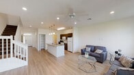 This two-story residence offers a thoughtfully designed open-concept floor plan with clean, contemporary finishes throughout. The main level begins with a bright, welcoming hallway finished with light wood-style flooring and recessed lighting, with a convenient half bath tucked nearby. The hallway opens into a generous living and dining area bathed in natural light from large windows, complete with a ceiling fan and smooth, neutral-toned walls. The kitchen is a functional centerpiece, featuring dark wood cabinetry, granite countertops, a kitchen island with an undermount sink, white appliances, pendant lighting, and a walk-in pantry for ample storage. A staircase with a white balustrade connects the two floors. Upstairs, the bedrooms are carpeted and generously proportioned. The primary bedroom is a standout, offering a sliding glass door to an outdoor balcony with views of the surrounding greenery and neighborhood. It includes an en-suite bathroom with a dual-sink vanity, dark wood cabinetry, light stone countertops, and a separate water closet. An additional bedroom also enjoys outdoor views through a large window. A secondary full bathroom with a shower-tub combination and single vanity serves the remaining rooms. The overall ambiance is bright, airy, and move-in ready.