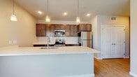 This single-floor residence offers a well-designed open-concept layout that seamlessly connects the kitchen and living areas. The kitchen is a standout feature, showcasing rich dark-stained cabinetry with ample upper and lower storage, a classic white subway tile backsplash, and a full suite of stainless steel appliances including a refrigerator, electric range, and built-in microwave. A generously sized island with a crisp white countertop and an integrated sink serves as both a functional workspace and a natural gathering point, illuminated by pendant lighting above.

The living area is bright and open, finished with light hardwood-style flooring that extends throughout the main space. Large windows and a sliding glass door provide natural light and direct access to a private balcony with outdoor views. The bedrooms are carpeted for comfort, each featuring windows that bring in additional natural light. The bathroom is clean and functional, featuring wood-look flooring, a tub-shower combination with brushed nickel fixtures, and a vanity with dark cabinetry. Neutral wall tones throughout create a cohesive, modern ambiance.