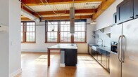 Located at 340 Rutgers St in Rochester's vibrant 14607 neighborhood, Unit 403 is a thoughtfully designed loft-style space that masterfully blends industrial character with modern finishes. The open layout is anchored by rich hardwood floors and striking exposed wood beam ceilings, lending warmth and architectural interest throughout.

The living area is bathed in natural light through large, wood-framed multi-pane windows that frame views of the surrounding neighborhood's rooftops and greenery. Whitewashed brick walls and pendant lighting enhance the loft aesthetic, creating an airy, open ambiance.

The kitchen is a standout feature, equipped with stainless steel appliances including a side-by-side refrigerator and a range with a sleek hood. Dark cabinetry, subway tile backsplash, stainless open shelving, and a stainless farmhouse sink combine to create a functional and stylish culinary space, with additional natural light from a large window.

The two bathrooms offer distinct finishes. One features a long double-sink vanity with a rich wood base, stone countertops, large-format tile flooring, and wall sconce lighting. The second bathroom includes a tiled walk-in shower with classic white subway tile walls and black penny tile flooring. Together, these spaces reflect a consistent attention to quality and design found throughout the entire unit.