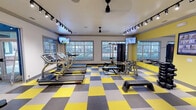 Located at 2650 Western Center Blvd in Fort Worth, Texas, this well-equipped fitness center is designed to support a comprehensive workout experience. The single-floor facility features a bold and energetic aesthetic, with a striking yellow, gray, and white checkered floor that sets a dynamic tone throughout the space. Track lighting and ceiling fans are mounted overhead, ensuring the room stays well-lit and comfortable during exercise.

The cardio zone is furnished with multiple treadmills and stationary bikes, positioned near large windows that invite natural light and provide views of the surrounding outdoor greenery. Flat-screen TVs are mounted on the walls, offering entertainment during workouts. The strength training area includes a multi-station cable machine, a weight bench, a dumbbell rack with free weights, and a step platform, providing a variety of resistance and functional training options.

Large glass sliding doors connect the fitness center to an adjacent lounge or common area, enhancing the open, integrated feel of the facility. A water fountain and sanitation station are conveniently located within the space. Wall-mounted mirrors further open up the room visually. The overall ambiance is clean, modern, and motivating, making this fitness center a functional and inviting amenity.