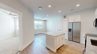This thoughtfully designed 1-bedroom, 1-bathroom unit offers a clean, modern aesthetic across its single floor. The open-concept kitchen and living area form the heart of the space, featuring light hardwood-style flooring, recessed lighting, and a ceiling fan that enhances airflow and comfort. The kitchen is well-equipped with a full suite of stainless steel appliances, including a French door refrigerator with ice and water dispenser, electric range, microwave, and dishwasher. Crisp white shaker cabinetry extends to the ceiling, providing ample storage, while light granite countertops and a subway tile backsplash add refined detail. A central kitchen island with matching granite offers additional prep space and casual seating potential. The living area benefits from natural light through a window with blinds. The bedroom is carpeted for comfort, features its own ceiling fan, and is served by a dedicated closet. The bathroom is clean and bright, showcasing wood-look tile flooring, a granite-topped vanity with modern hardware, a tub-shower combination with marble-style tile surround, and generous built-in storage cabinetry — creating a functional and polished finishing touch to this efficiently laid-out home.