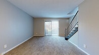 Located at 1000 S Woodlawn Blvd in Wichita, Kansas, this two-story residence offers a well-organized layout spread across two levels. The main floor features a generously sized living area finished with neutral-toned carpet and soft gray walls, bathed in natural light through a full sliding glass door fitted with vertical blinds. A staircase with distinctive decorative iron railings rises from the living space, serving as both a functional and visual centerpiece of the main floor. The kitchen is equipped with dark cabinetry, stainless steel appliances including a full-size refrigerator, light stone countertops, and durable wood-look flooring, with a window providing additional natural light. A pass-through window connects the kitchen to an adjacent carpeted living or dining area, enhancing the open feel between spaces. Upstairs, the bedrooms are carpeted and well-lit, each featuring ceiling fans and access to natural light through windows or sliding glass doors with vertical blinds. One bedroom includes generous built-in closet storage with double doors along an entire wall. Throughout the home, the neutral color palette, consistent carpeting, and clean white trim create a cohesive, move-in-ready environment suited for comfortable everyday living.