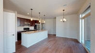 This single-floor residence is thoughtfully designed with an open-concept layout that connects the kitchen and living area into one cohesive, generously sized space. The kitchen is a functional centerpiece, outfitted with rich, dark espresso cabinetry, stainless steel appliances including a refrigerator, range, and over-the-range microwave, and granite-style countertops that extend across a large island with a double-basin sink. A tile backsplash adds texture behind the range, while pendant lighting above the island and a chandelier in the adjoining living area provide warm, layered illumination. Durable hardwood-style flooring runs throughout the main living spaces, complementing the neutral wall tones.

The bedrooms are carpeted for comfort and feature ceiling fans, natural light from windows with blinds, and access to walk-in closets with built-in rod systems. Two bathrooms mirror each other in finish quality, each featuring dark wood vanities with white countertops, framed mirrors, and tile or hardwood-style flooring. A dedicated laundry area is visible near the kitchen. The overall aesthetic is clean, modern, and consistent, with neutral tones and coordinated finishes creating a cohesive environment throughout.