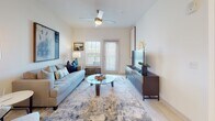 This single-floor residence offers a well-designed layout that balances comfort and functionality across its living spaces. The living room serves as the heart of the home, featuring light-toned flooring, a ceiling fan with lighting, and a glass-panel exterior door flanked by windows dressed with plantation shutters, allowing ample natural light to fill the space. The room comfortably accommodates a tufted sofa, glass-top coffee table, and media console, creating a cohesive and inviting atmosphere.

The kitchen is outfitted with white shaker-style cabinetry extending to the ceiling, a white subway tile backsplash, light countertops, and a full suite of stainless steel appliances including a refrigerator, electric range, microwave, and dishwasher. Light wood-style flooring completes the clean, contemporary aesthetic.

The two bedrooms are carpeted and well-proportioned, each featuring ceiling fans or overhead lighting and windows with plantation shutters or sheer curtains for natural light and privacy. A walk-in closet with multi-tier shelving and hanging rods provides generous storage.

The bathroom presents a minimalist design with a glass-enclosed walk-in shower featuring white tile surround, light tile flooring, and clean white walls throughout.