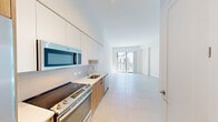 Located at 999 NW Seventh St in Miami, FL, this efficiently designed single-floor unit offers a bright, contemporary living experience. The open-plan layout seamlessly connects the kitchen and living area, creating a sense of spaciousness despite its compact footprint. Large sliding glass doors flood the living space with natural light and open onto a private outdoor area, offering views of the surrounding urban landscape.

The kitchen is thoughtfully designed with a combination of white upper cabinetry and warm wood-toned lower cabinets, complemented by a white tile backsplash and light stone countertops. A full suite of stainless steel appliances — including a refrigerator, electric range, built-in microwave, and dishwasher — provides modern convenience. Light-toned large-format tile flooring runs throughout, reinforcing the clean, cohesive aesthetic.

The bathroom features floor-to-ceiling white tile with a classic vertical grout pattern, creating a crisp, clean atmosphere around the bathtub-shower combination. A well-proportioned entry corridor with clean white walls and neutral tile connects all areas of the unit. The overall design is defined by a minimalist palette of whites and natural wood tones, delivering a fresh, modern ambiance well-suited to Miami's contemporary urban living environment.