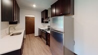 Located at 2050 Delaware Ave in West St. Paul, Minnesota, this single-floor unit offers a well-organized and functional layout designed for comfortable everyday living. The kitchen is a standout feature, showcasing rich dark espresso cabinetry, light quartz countertops, a peninsula with an undermount sink, stainless steel appliances including a refrigerator and range, a tile backsplash, and a sleek range hood — all set atop durable wood-look vinyl flooring. The kitchen opens directly to the living area, which transitions from wood-look flooring to plush carpeting, creating a warm and inviting atmosphere. A ceiling fan with light fixture and a window offering outdoor views are also featured in the living space, along with baseboard heating and a wall-mounted air conditioning unit for year-round comfort. The bedroom is generously sized with soft carpet flooring, clean white walls, and easy access to the hallway. The full bathroom is neatly appointed with dark wood cabinetry, a white countertop vanity, a wall-mounted medicine cabinet, large mirror, and a tiled tub-shower combination. A separate half bath with a clean vanity and mirror adds additional convenience. Warm wood-toned doors and trim throughout tie the space together with a cohesive, classic aesthetic.
