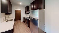 Located at 2050 Delaware Ave in West St. Paul, Minnesota, this single-floor unit offers a well-organized and functional layout designed for comfortable everyday living. The kitchen is a standout feature, showcasing rich dark espresso cabinetry, light quartz countertops, a peninsula with an undermount sink, stainless steel appliances including a refrigerator and range, a tile backsplash, and a sleek range hood — all set atop durable wood-look vinyl flooring. The kitchen opens directly to the living area, which transitions from wood-look flooring to plush carpeting, creating a warm and inviting atmosphere. A ceiling fan with light fixture and a window offering outdoor views are also featured in the living space, along with baseboard heating and a wall-mounted air conditioning unit for year-round comfort. The bedroom is generously sized with soft carpet flooring, clean white walls, and easy access to the hallway. The full bathroom is neatly appointed with dark wood cabinetry, a white countertop vanity, a wall-mounted medicine cabinet, large mirror, and a tiled tub-shower combination. A separate half bath with a clean vanity and mirror adds additional convenience. Warm wood-toned doors and trim throughout tie the space together with a cohesive, classic aesthetic.