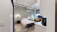 Located at 305 Michigan Ave in the heart of Detroit, this efficiently designed studio unit offers a thoughtfully arranged open-concept layout that combines the living, dining, and kitchen areas into one cohesive space. The interior showcases a contemporary industrial aesthetic, highlighted by exposed ductwork, rail track lighting suspended from elevated ceilings, and light wood-tone flooring throughout.

The kitchen is fully equipped with stainless steel appliances — including a full-size refrigerator, range, microwave, and dishwasher — complemented by crisp white cabinetry and a clean white countertop. A compact dining area with a round wood table and modern chairs sits adjacent, making the most of the open floor plan.

The sleeping area features a ceiling fan, a wall-mounted mini-split HVAC unit, and a sage green accent wall that adds a calming, grounded tone to the space. Natural light enters through a window fitted with roller shades.

The bathroom offers a clean, modern vanity with white cabinetry and gold hardware, while a separate laundry area and closet provide practical storage and in-unit convenience. Every element of this studio is designed to maximize functionality within a compact, well-appointed urban living space.