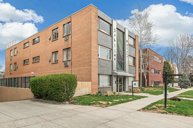Inviting brick apartment building with modern facade and lush landscaping under a bright blue sky. - Sublime