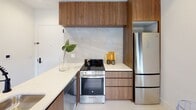 Located in Newark, NJ, this Clinton Flats one-bedroom, one-bathroom residence offers a well-designed single-floor layout that blends modern aesthetics with functional living. The living area is a standout space, anchored by large wood-framed windows topped with leaded transom panes that flood the room with natural light while framing elevated views of the surrounding cityscape. Light hardwood flooring runs throughout, complementing the bright, neutral palette.

The kitchen is outfitted with warm walnut cabinetry extending to the ceiling, sleek white quartz countertops, a marble-look stone backsplash, and stainless steel appliances including a full-size range and refrigerator. The entry foyer, adjacent to the kitchen, continues the wood cabinetry detail and features clean white walls with matte black hardware accents.

The bedroom mirrors the living area's aesthetic with tall ceilings, wood-framed windows with upper transom glazing, and a calm, restful atmosphere. The bathroom showcases a bold yet refined design with full-height white subway tile walls, a striking terrazzo-style mosaic floor, a walnut vanity, and matte black fixtures and accessories throughout. This residence delivers a cohesive, contemporary living experience in the heart of Newark.