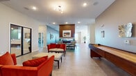 This single-floor amenity center is thoughtfully designed to support a wide range of activities within a cohesive, modern aesthetic. The expansive main lounge serves as the heart of the space, featuring bold red upholstered seating, a wood-paneled fireplace surround, and a shuffleboard table, all set against light tile flooring and recessed lighting. A sputnik-style ceiling fixture adds a retro-modern touch. This area flows seamlessly into the game room, which showcases a full-size pool table centered on a vibrant geometric area rug, a wall-mounted flat-screen TV above the fireplace, and casual seating along gray textured walls.

The fitness facilities are split into two distinct zones: one equipped with treadmills, free weights, and a weight bench on rubberized flooring, and a second, more dynamic studio featuring colorful striped wall murals, exercise balls, resistance equipment, and cardio machines with outdoor views.

The fully equipped kitchen includes stainless steel appliances, white cabinetry, a patterned tile backsplash, open shelving, and a bar-height island with pendant lighting. Adjacent meeting rooms offer carpet flooring, teal and green accent walls, wall-mounted displays, and glass sliding doors, providing functional collaborative spaces throughout.