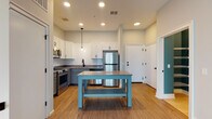 Located at 750 E Broad St in Columbus, Ohio, this single-floor unit offers a thoughtfully designed layout with modern finishes throughout. The kitchen serves as a central highlight, featuring two-tone cabinetry — white upper cabinets paired with gray lower cabinets — complemented by quartz countertops, a white subway tile backsplash, stainless steel appliances including a refrigerator, range, microwave, and dishwasher, and a freestanding island that provides additional prep and dining space. Pendant lighting adds a warm, contemporary touch overhead. An open-concept flow connects the kitchen to the living area, which is bathed in natural light from large sliding glass doors fitted with vertical blinds. A dedicated in-unit laundry closet with a stacked washer and dryer adds everyday convenience. The bedrooms are carpeted and generously sized, each featuring windows with views of surrounding greenery. A spacious walk-in closet with wire shelving provides ample storage. The bathroom is finished with teal accent walls, matte black fixtures, a white vanity with a dark countertop, and a full tub-shower combination. Light wood-look flooring runs throughout the main living areas, tying the design together cohesively.
