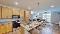 Located in Clayton, NC, this single-floor residence offers a well-designed open-concept layout that seamlessly connects the kitchen, dining, and living areas. The kitchen is a standout feature, equipped with stainless steel appliances including a French door refrigerator, electric range, and built-in microwave. Warm-toned maple cabinetry provides generous storage, while granite countertops extend across both the perimeter workspace and a central island fitted with an undermount sink and bar seating — ideal for casual dining or entertaining. Pendant lighting above the island adds a refined touch. Light hardwood flooring runs throughout the main living areas, complementing the crown molding and recessed lighting that lend a polished finish to the space. The living room is bright and inviting, anchored by French doors with transom windows that welcome natural light and provide outdoor views, along with a ceiling fan for year-round comfort. The bedroom is a calm retreat featuring plush carpet, a ceiling fan, and a window with exterior views. The bathroom includes a granite-topped vanity, hardwood-style flooring, and a full soaking tub with shower. Together, these spaces create a cohesive, comfortable home with quality finishes throughout.