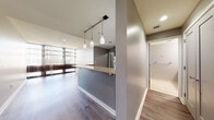 Located on the ninth floor at 400 S Fourth Street in downtown St. Louis, Missouri, this single-level unit features a thoughtfully designed open-concept layout that blends the kitchen and living areas seamlessly. The kitchen is equipped with stainless steel appliances, including a full-size refrigerator and electric range, complemented by rich dark wood cabinetry with ample storage and granite-style countertops. A peninsula-style breakfast bar with pendant lighting serves as both a functional workspace and a casual dining area, anchoring the transition between the kitchen and living space. The living area is highlighted by wide-plank hardwood-style flooring and floor-to-ceiling windows dressed with vertical blinds, allowing generous natural light and city views to fill the room. The bedroom features plush carpeting, neutral gray walls, and direct access to the hallway corridor. A tiled bathroom and additional storage areas are accessible from the central hallway. Throughout the unit, a consistent neutral color palette of soft grays and warm wood tones creates a cohesive, modern aesthetic. Recessed lighting and track pendant fixtures provide well-distributed illumination across each area, enhancing the clean, contemporary feel of this downtown St. Louis residence.