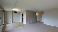 Located at 25 Washington Lane in Wyncote, Pennsylvania, this single-floor residence offers a clean, modern aesthetic defined by an open and airy layout. The interior is finished in soft, neutral gray tones throughout, creating a calm and cohesive atmosphere that feels both inviting and contemporary.

The main living area is generously proportioned, combining light hardwood-style flooring in the dining and entry zones with plush carpeting in the living space, providing both warmth and visual distinction between areas. A sleek drum pendant light fixture anchors the dining area, adding a stylish focal point against the smooth white ceiling.

A central dividing wall segments the open floor plan, offering a natural separation between the living space and connecting hallways without sacrificing the overall sense of openness. Multiple doorways lead to additional rooms, including what appears to be a kitchen fitted with dark cabinetry, visible through an open entry.

Clean white baseboards and smooth walls throughout contribute to the polished, well-maintained appearance of the space. The layout flows intuitively, with corridors connecting the main living areas to private spaces beyond. The overall design prioritizes simplicity and functionality, making this a versatile and move-in ready single-floor home in the Wyncote community.