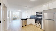 Located at 855 Main St in downtown Bridgeport, CT, this thoughtfully designed unit offers a well-organized single-floor layout encompassing a kitchen and living area, a separate living room, and a full bathroom. The open-concept kitchen and living area is a standout feature, showcasing white shaker cabinetry with gold hardware, dark countertops with a tile backsplash, a peninsula with a built-in sink, and a full suite of stainless steel appliances including a range, microwave, dishwasher, and refrigerator. A modern ring pendant light fixture adds a stylish focal point overhead. Light wood-tone flooring flows consistently throughout the unit, complementing the clean white walls and creating a bright, cohesive aesthetic. The living room benefits from expansive floor-to-ceiling windows that frame sweeping views of the Bridgeport skyline and surrounding urban landscape, flooding the space with natural light. The bathroom is finished with neutral tile walls and flooring, matte black fixtures, and a full soaking tub with shower. A dedicated entry area near the front door provides a practical transition space. The unit's modern design, city views, and quality finishes make it a polished urban residence.