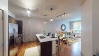 This well-appointed single-floor residence offers a thoughtfully designed open-concept layout that seamlessly connects the kitchen, dining, and living areas. The kitchen is a standout feature, showcasing dark espresso cabinetry, stainless steel appliances including a French door refrigerator and electric range, a subway tile backsplash, and a generous island with a quartz countertop and integrated sink. Globe pendant lights and a track lighting system illuminate the space with a warm, modern glow, while warm-toned hardwood flooring flows throughout the main living areas.

The living room is bright and inviting, anchored by a textured accent wall with a subtle wave pattern and a large window that draws in natural light and outdoor views. The dining area connects fluidly between the kitchen island and the living space, creating an ideal layout for entertaining.

The bedrooms are comfortably sized, each featuring ceiling fans, generous windows with views of the surrounding neighborhood, and carpeted flooring for added comfort. The bathroom is finished with a dark vanity cabinet topped with a marble-style countertop, a framed mirror with warm Edison-style vanity lighting, and a glass-enclosed walk-in shower with tile surround. The overall ambiance is contemporary and refined, with cohesive finishes throughout.