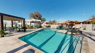 This upscale residential complex boasts a centerpiece resort-style pool area that exemplifies luxury living in the Southwest. The expansive pool, with its crystal-clear turquoise water, is the focal point of the community's outdoor amenities. Surrounding the pool are comfortable lounge chairs and umbrellas, perfect for relaxation and sunbathing. The area is further enhanced by cabanas and pergolas, providing shaded retreats from the Arizona sun.

The architectural style of the buildings reflects a modern interpretation of traditional southwestern design, with clean lines and flat roofs. The structures are painted in a crisp white, creating a striking contrast against the vibrant blue sky. Palm trees and other desert-adapted plants dot the landscape, adding a touch of natural beauty to the meticulously maintained grounds.

Multiple seating areas and gathering spaces are scattered throughout, encouraging social interaction among residents. The community appears to offer a blend of private residences and common areas, fostering a sense of community while maintaining individual privacy. The overall ambiance is one of refined relaxation, perfectly suited to the Tucson climate and lifestyle.