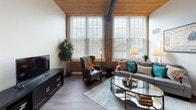 Located at 80 Mechanic St in Attleboro, Massachusetts, this single-floor loft-style residence masterfully blends industrial character with modern comfort. The living area is a standout, showcasing exposed brick walls, warm wood-plank ceilings with structural beams, and oversized multi-pane windows that flood the space with natural light and offer views of the surrounding neighborhood. Rich hardwood-style flooring runs throughout, tying the open layout together seamlessly.

The kitchen is thoughtfully designed with crisp white shaker cabinetry, stone-look countertops, and a full suite of stainless steel appliances, including a gas range, built-in microwave, refrigerator, and dishwasher — offering both style and functionality.

The bedrooms continue the loft aesthetic, with soaring ceilings accented by natural wood planking and exposed beams. Large windows bring in generous daylight, creating bright and airy retreats. Ample closet space adds practical storage to each room.

The bathroom features a clean, contemporary design with a white vanity, large mirror, and a tub-shower combination, maintaining the cohesive neutral palette found throughout the residence.

Overall, this space delivers a distinctive urban-industrial ambiance, highlighted by its architectural details and thoughtful modern finishes.